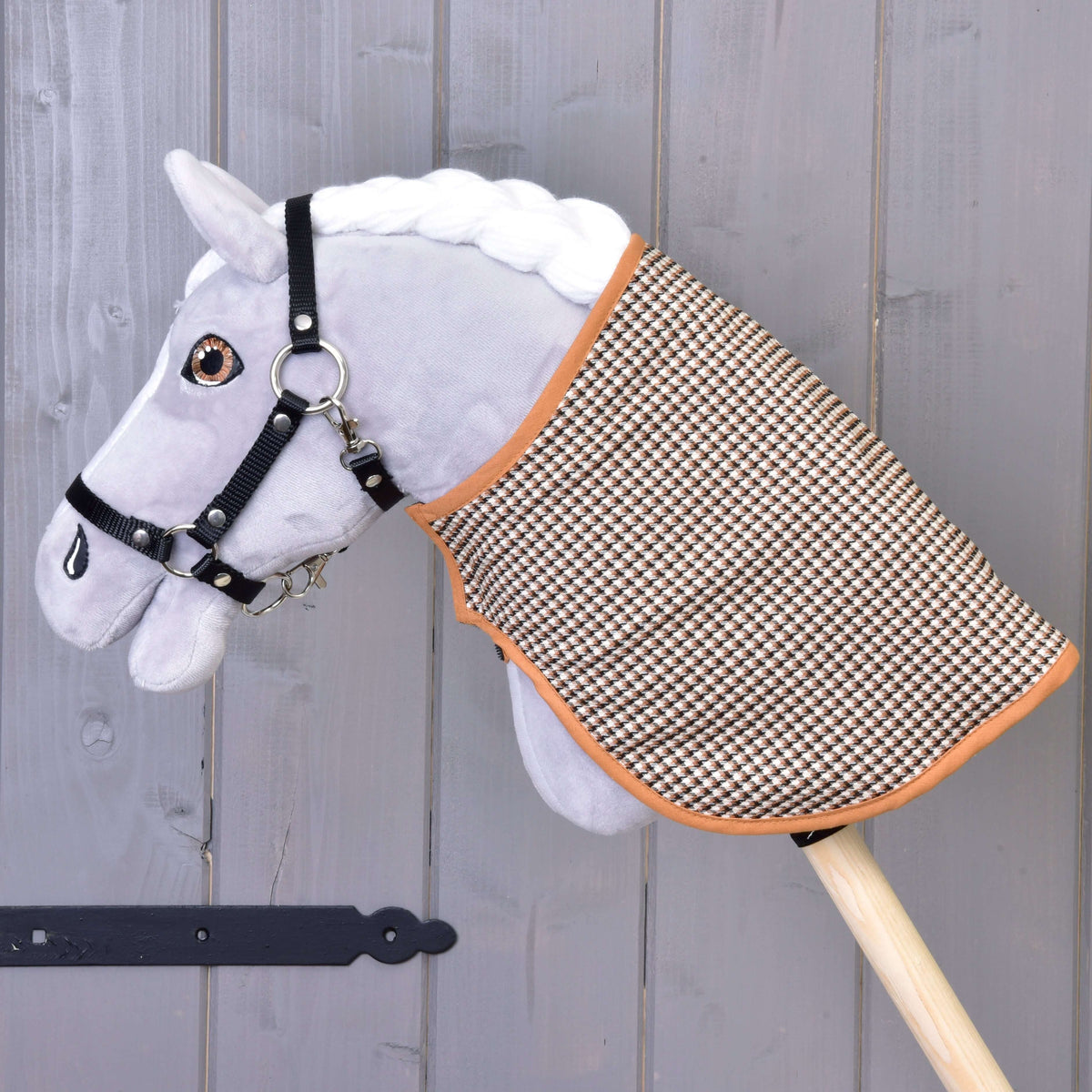 Een grijze pluche Hobby Horse met zwarte halster draagt de deken met de bruine pied-de-poule kant buiten voor een grijze wand