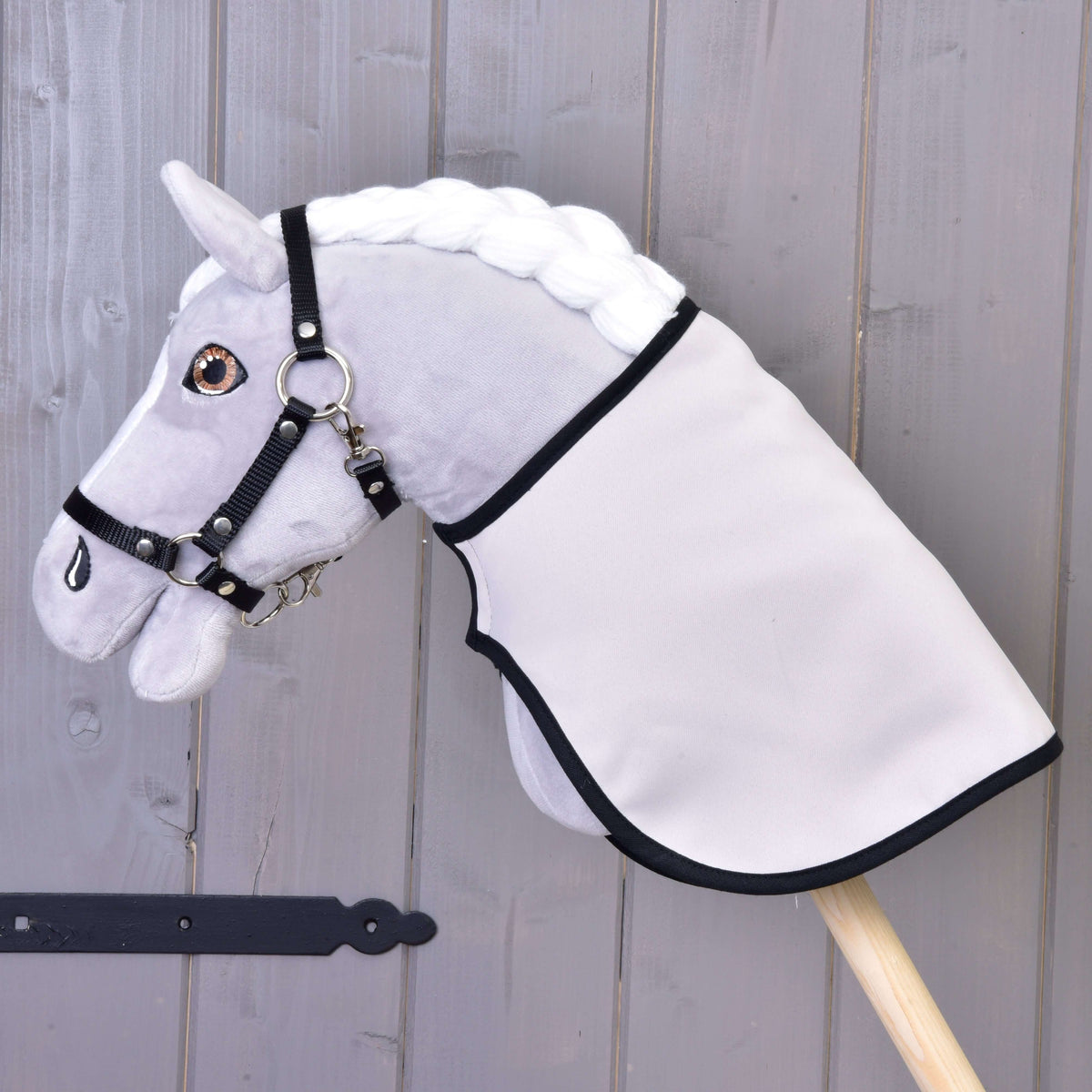 Een grijze pluche Hobby Horse met zwarte halster draagt de deken omgekeerd met de effen lichte kant buiten en zwarte bies