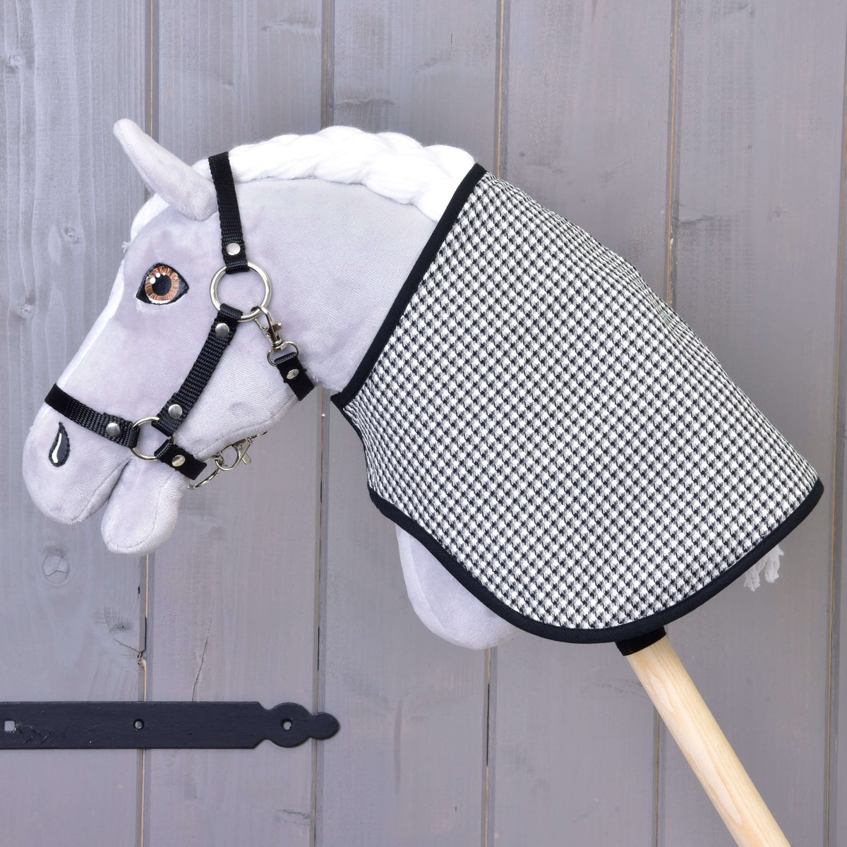 Een grijze pluche Hobby Horse met zwarte halster draagt de deken met de zwart-witte pied-de-poule kant buiten