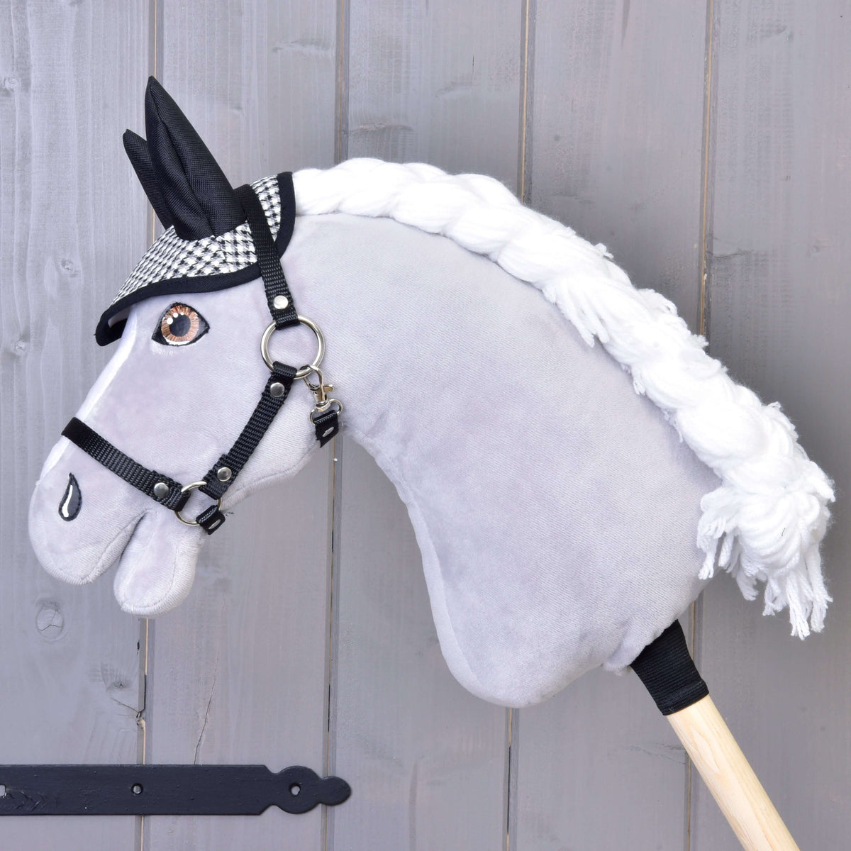Un Hobby Horse gris en peluche à crinière blanche tressée et licol noir porte le bonnet d’oreilles pied-de-poule noir et blanc