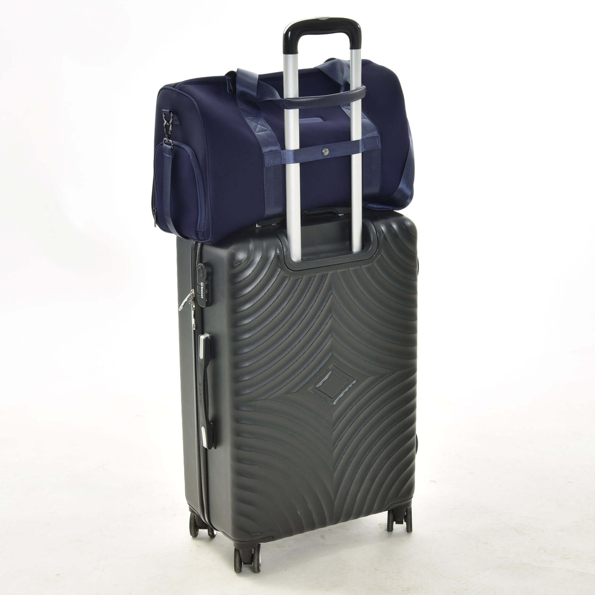 Sac de sport Hobby Horse bleu marine sur une valise noire à roulettes, sa sangle arrière glissée sur la poignée télescopique