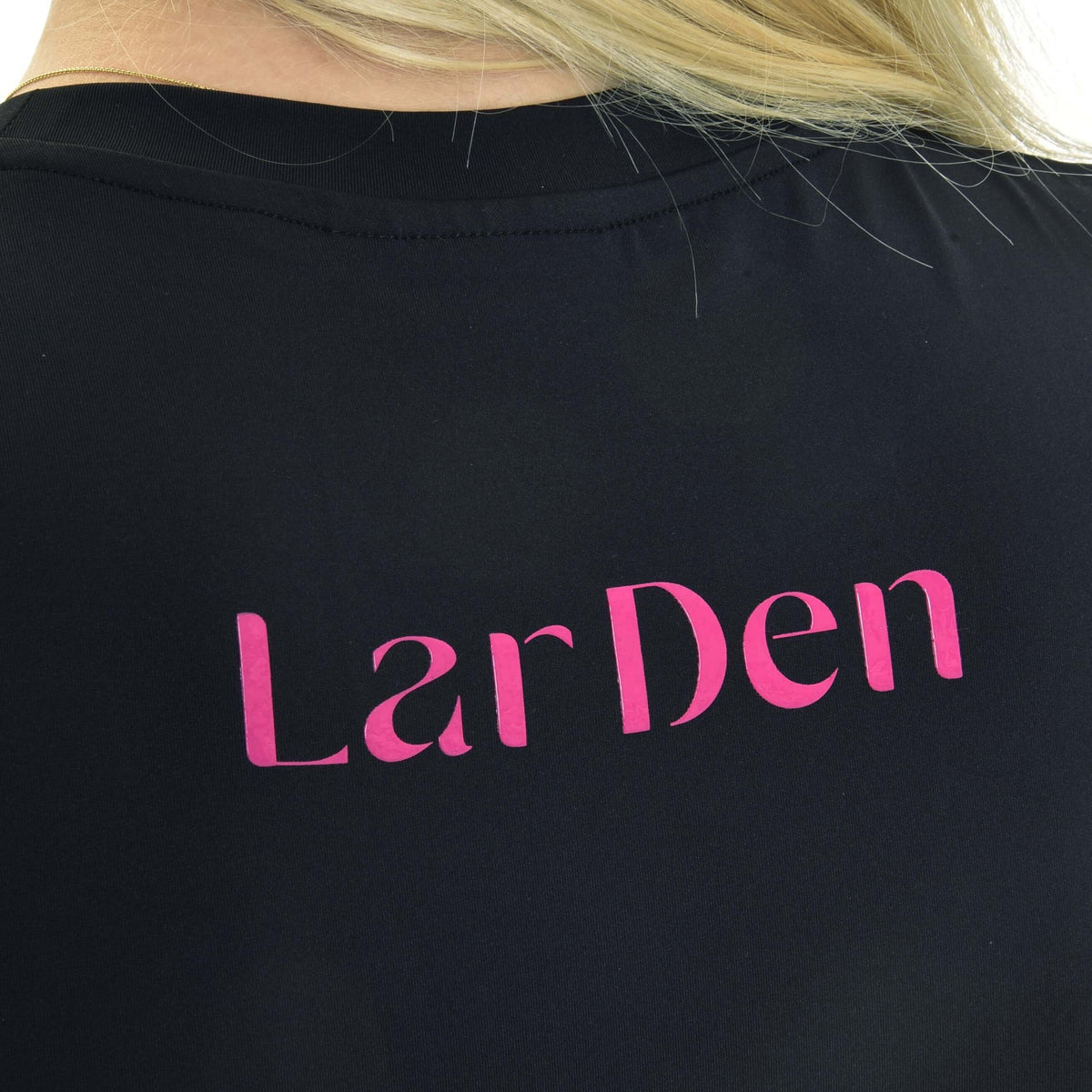 Close-up van de roze LarDen-letters op de rug van een zwart sportshirt met ronde hals, blond haar over de schouder