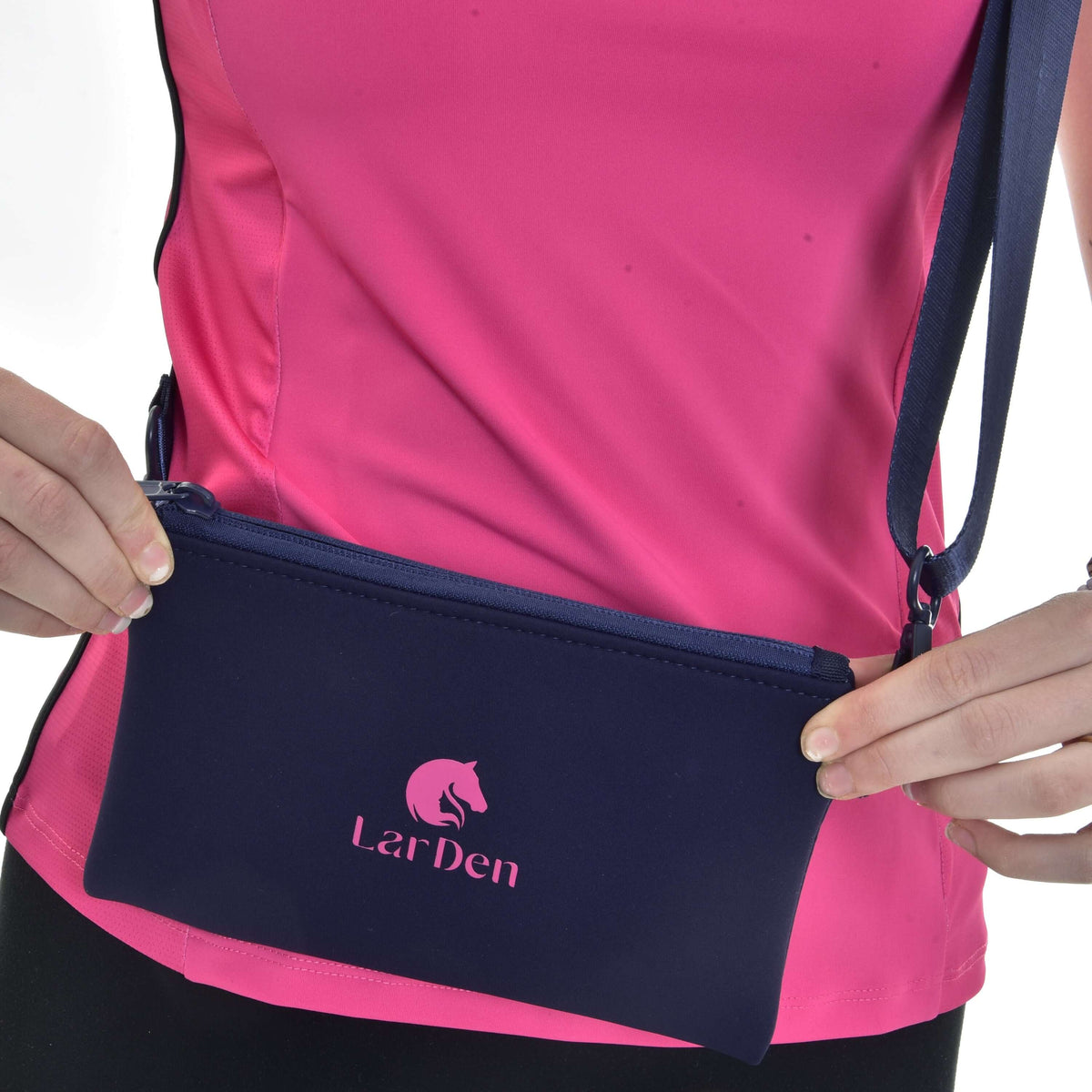 Gros plan de mains tenant le sac en bandoulière Hobby Horse à la hanche, logo rose LarDen sur néoprène bleu marine