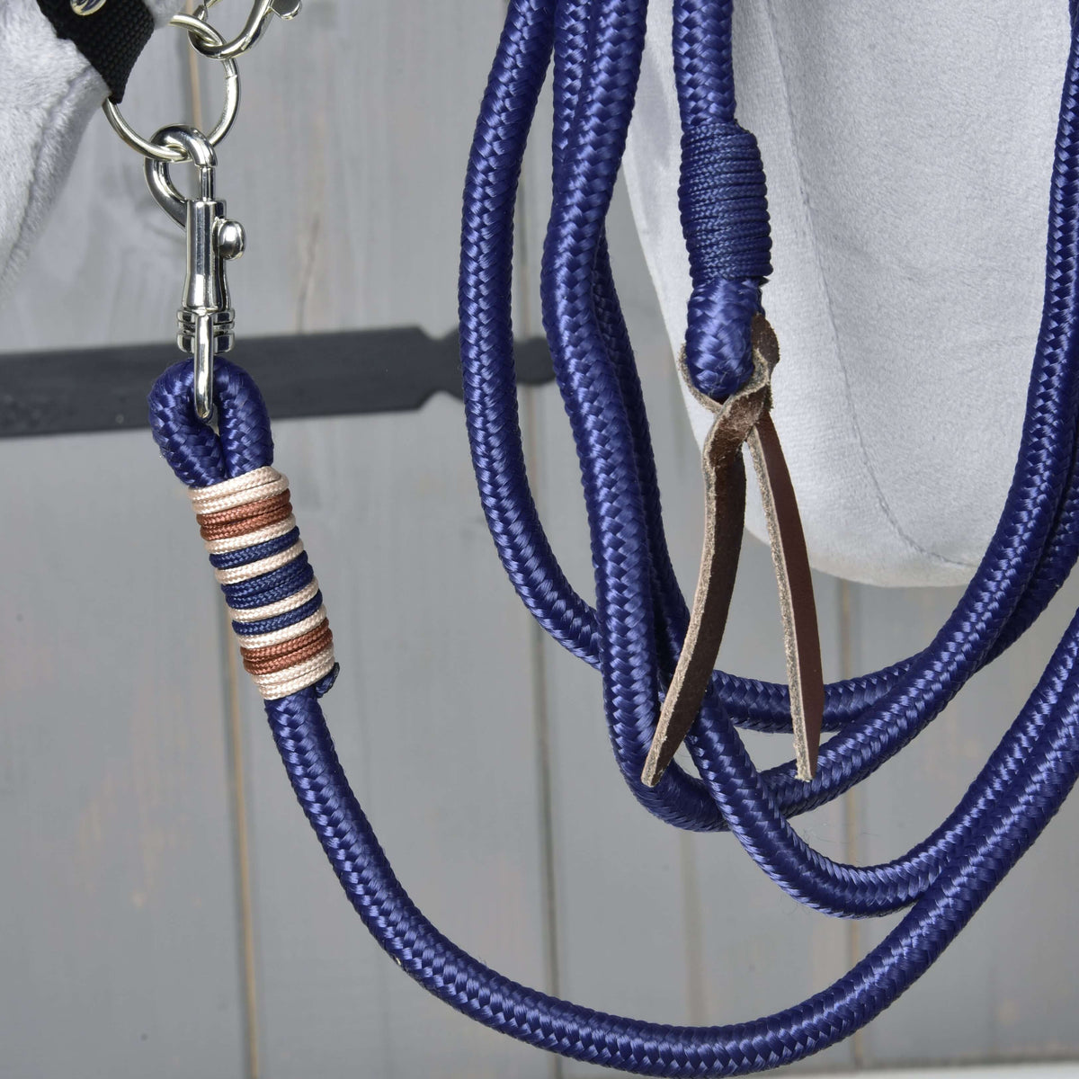 Close-up of the Hobby Horse Lunging Rope: silver snap hook, beige and brown thread wrap and leather popper on navy rope