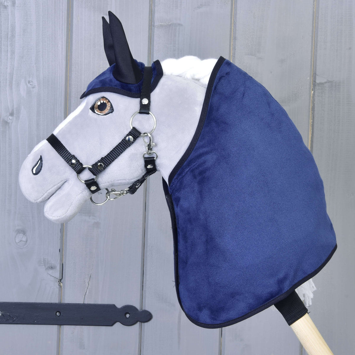 Grijze Hobby Horse met bruine ogen en zwart halster in de donkerblauwe fluweelachtige deken en het oornetje