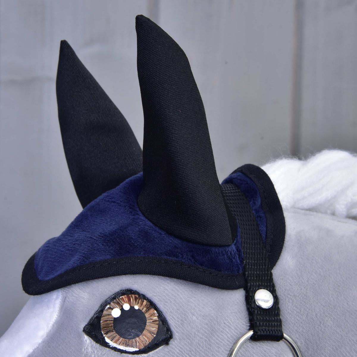Close-up van het donkerblauwe fluweelachtige oornetje met hoge zwarte oren en zwarte bies boven een bruin oog