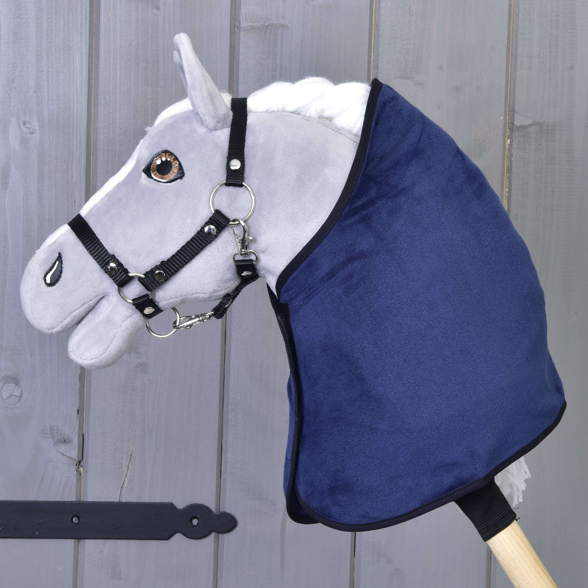 Grijze Hobby Horse met zwart halster die alleen de donkerblauwe fluweelachtige deken met zwarte bies draagt
