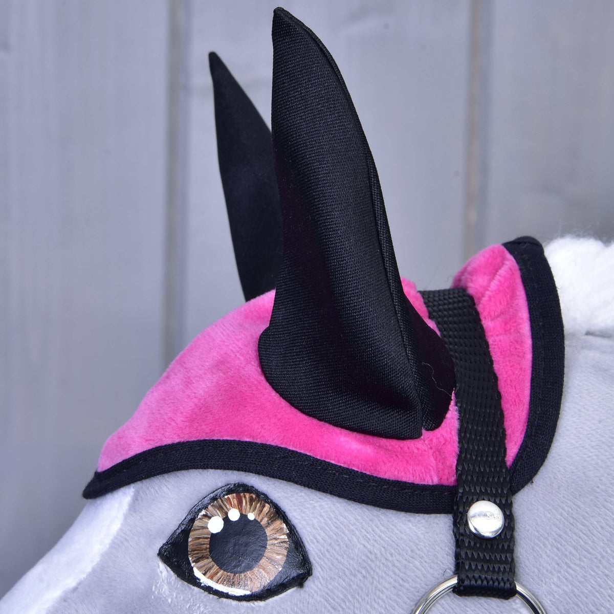 Gros plan sur le bonnet d'oreilles velouté rose vif aux oreilles noires et à bordure noire, au-dessus d'un œil marron