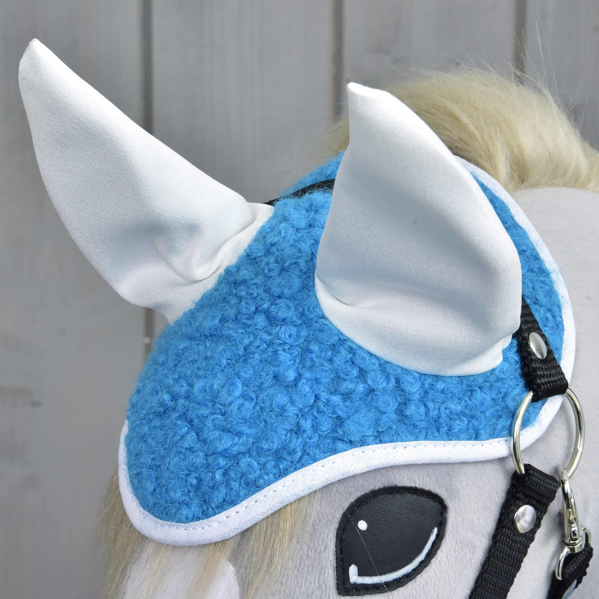 Close-up of the blue curly fleece ear bonnet with smooth white ear covers and white binding on a grey plush head