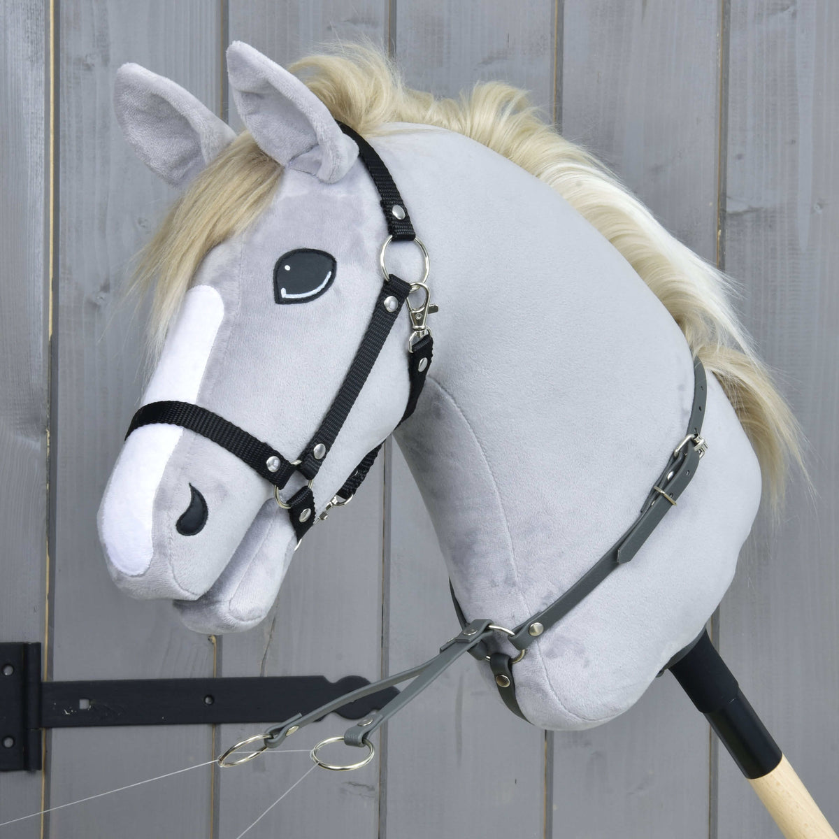 Grijze pluche Hobby Horse met zwarte halster en de donkergrijze martingaal om de hals, de twee ringen hangen naar voren