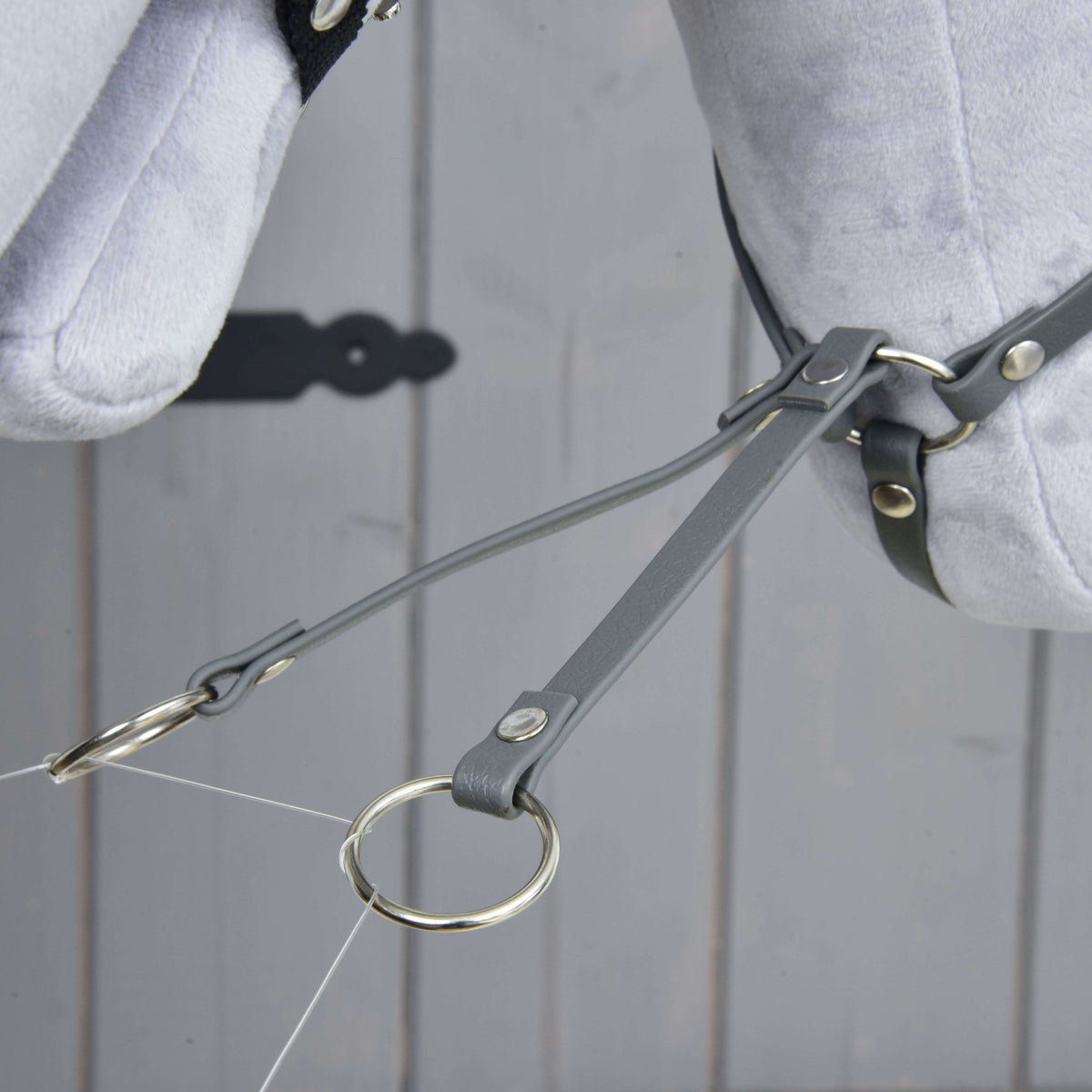 Close-up van de twee takken van de donkergrijze martingaal van kunstleer met zilveren ringen onder het pluche hoofd