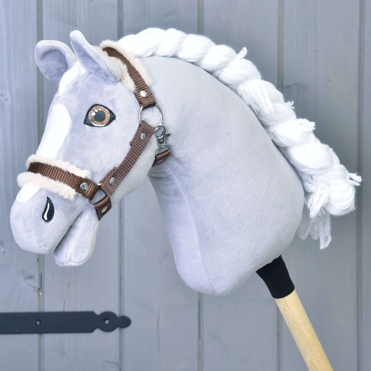 Een grijze pluche Hobby Horse met witte gevlochten manen en bruine ogen draagt de bruine halster met beige bont