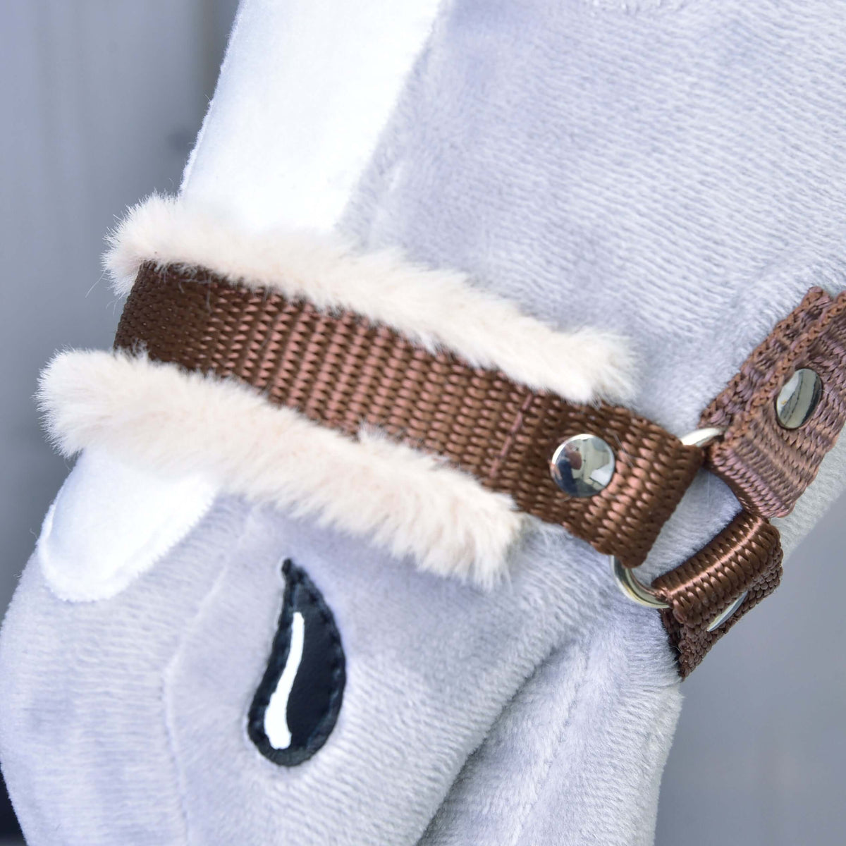 Close-up van de bruine neusriem met zacht beige bont en een zilveren klinknagel op een grijze pluche Hobby Horse