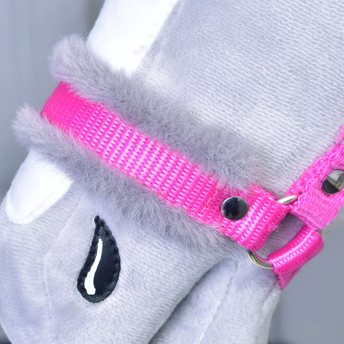 Gros plan sur la muserolle en sangle rose bordée de fourrure grise douce et son rivet argenté, sur un Hobby Horse gris en peluche