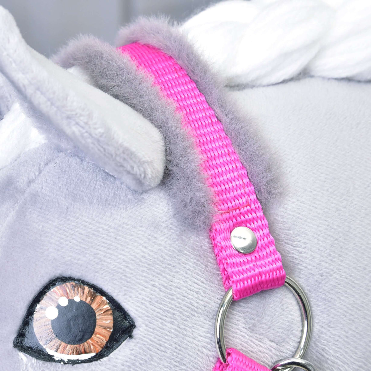 Gros plan sur la têtière rose à fourrure grise derrière l’oreille, l’anneau argenté et l’œil marron du Hobby Horse