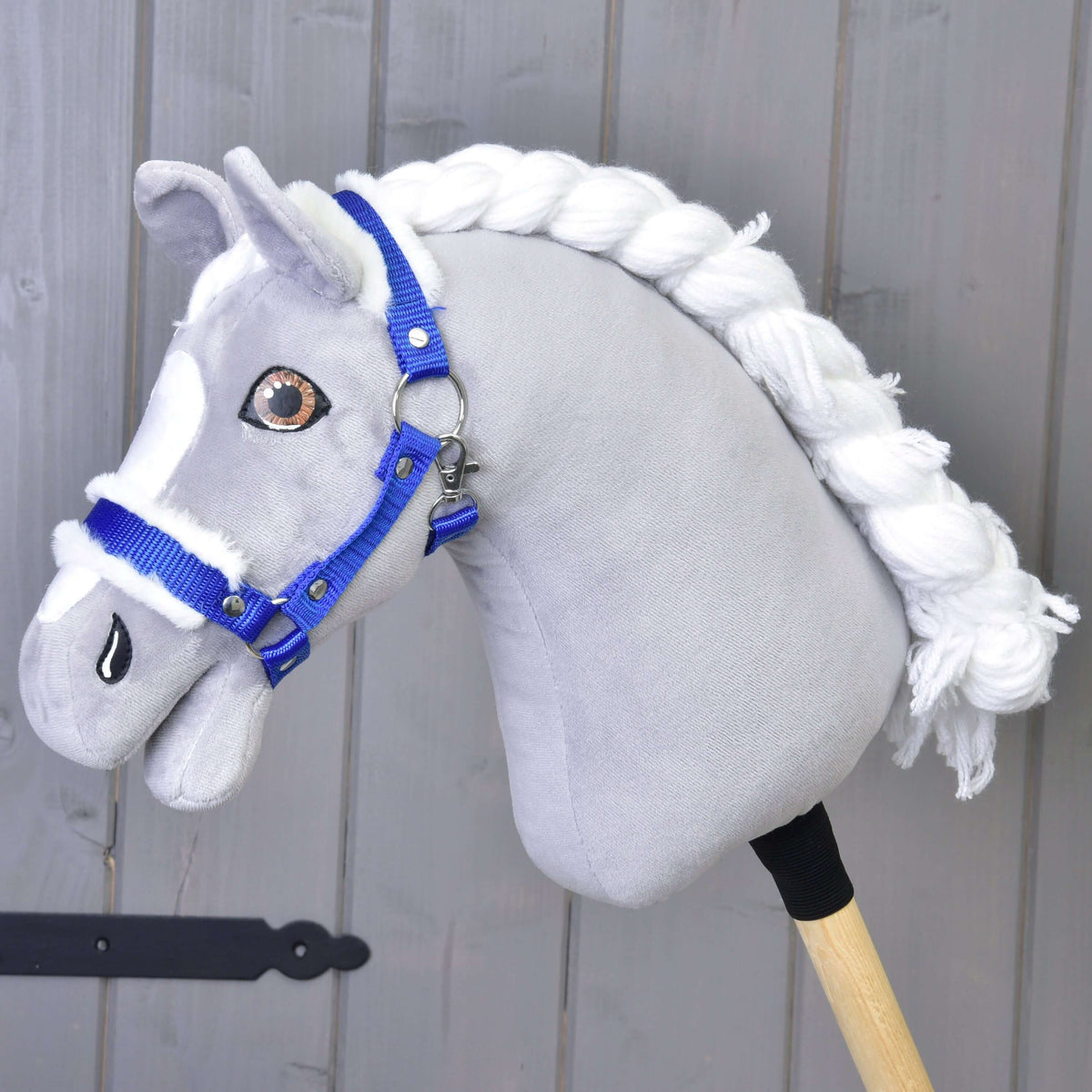 Een grijze pluche Hobby Horse met witte gevlochten manen en bruine ogen draagt de koningsblauwe halster met wit bont