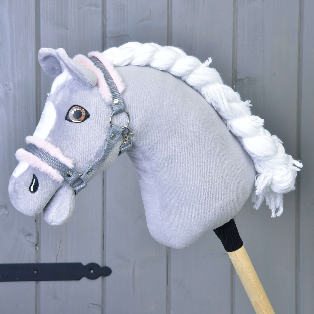 A grey plush Hobby Horse with a white braided mane and brown eyes wears the grey halter with light pink fur