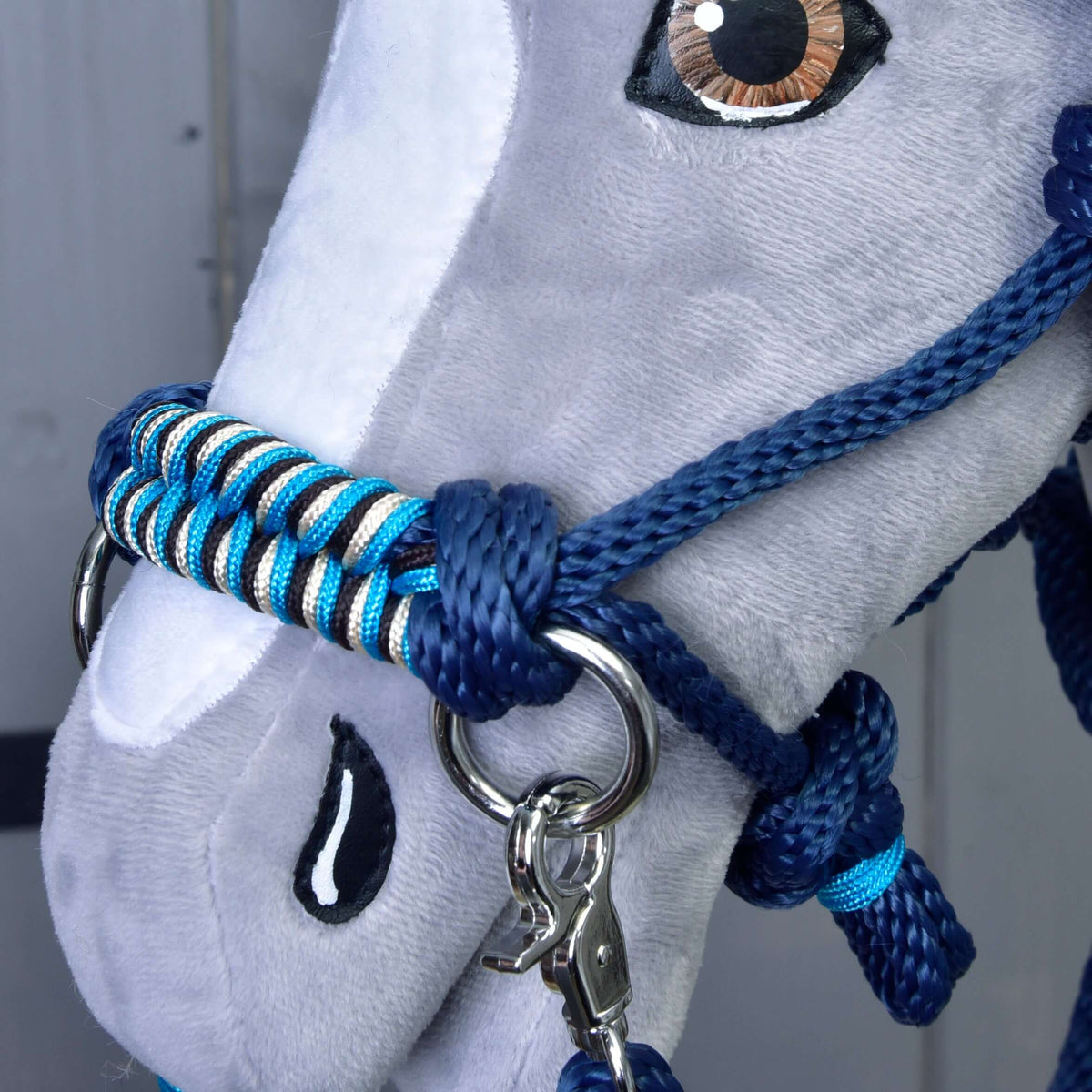 Close-up van de marineblauwe touwhalster op een grijze Hobby Horse met turquoise, zwart en crème gevlochten neusriem en musketon