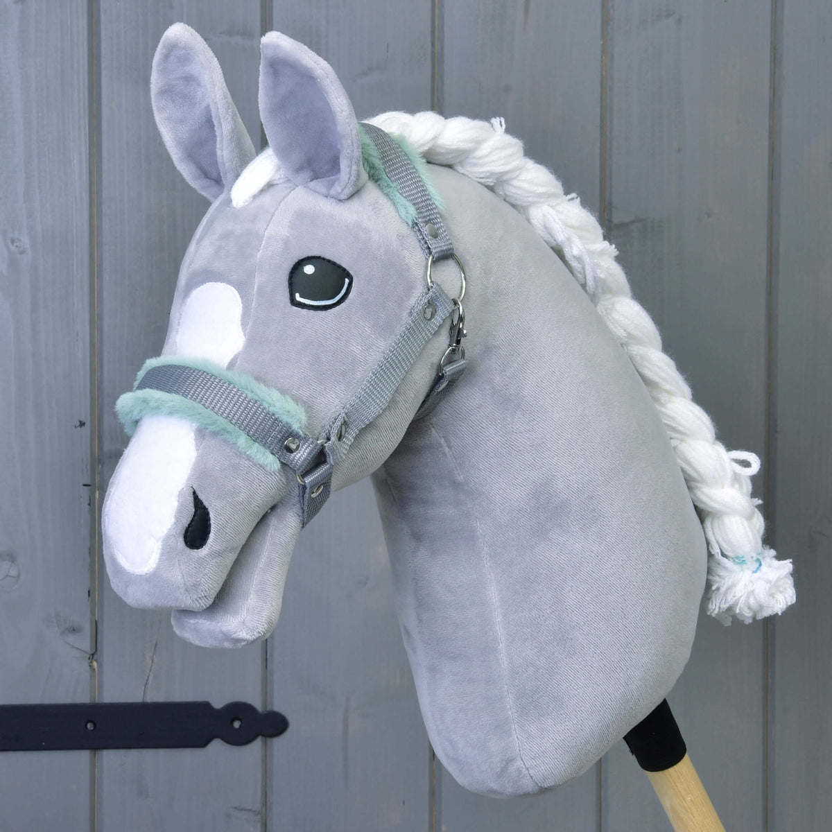 Een grijze pluche Hobby Horse met witte bles en gevlochten manen draagt de grijze halster met mintgroen bont