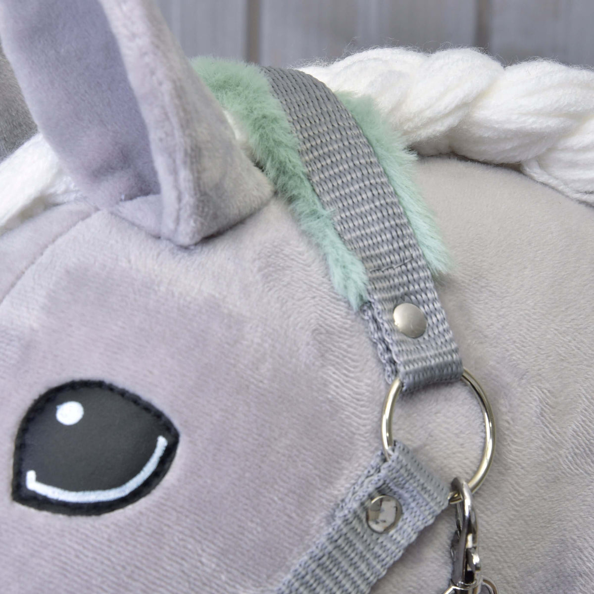 Close-up van het grijze kopstuk met mintgroen bont bij het oor en donkere oog van een grijze pluche Hobby Horse