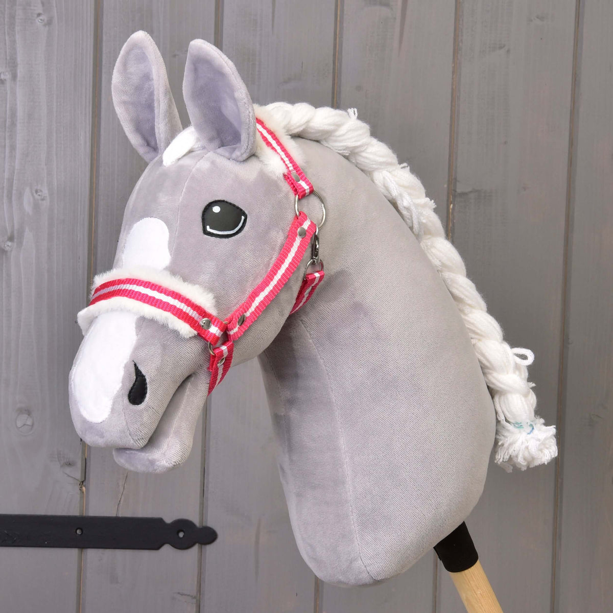 Een grijze pluche Hobby Horse met witte bles en gevlochten manen draagt de rood gestreepte halster met wit bont