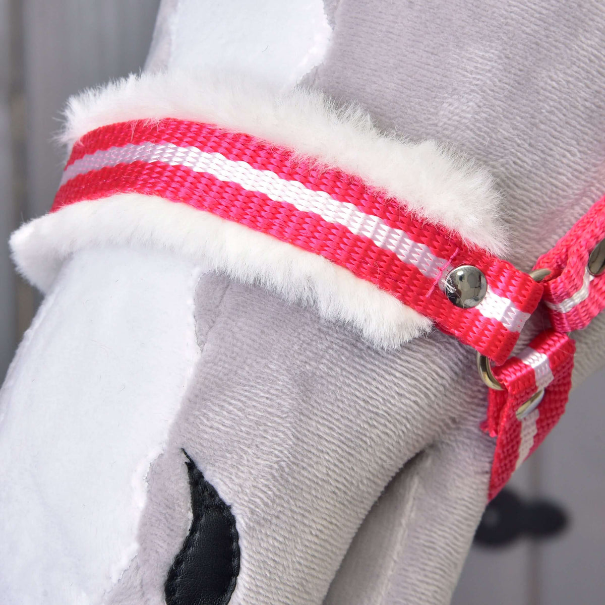 Close-up van de rood-wit gestreepte neusriem met zacht wit bont op een grijze pluche Hobby Horse