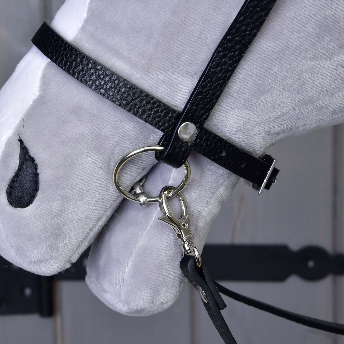 Close-up of the black leatherette noseband on a grey Hobby Horse with a silver ring, buckle and the snap hook of the reins