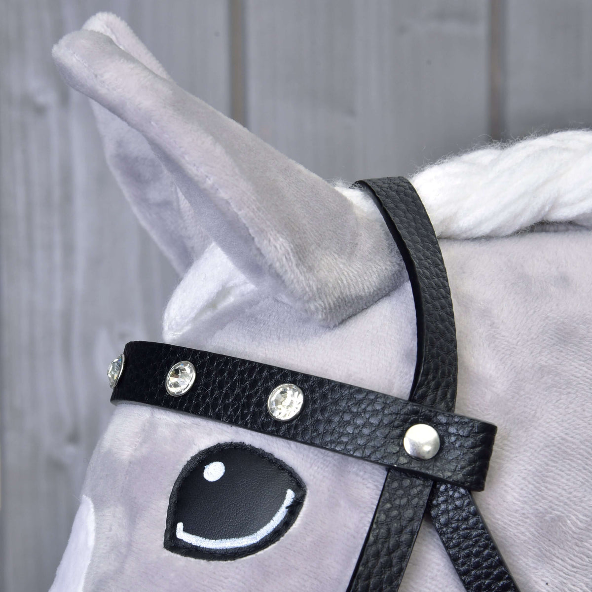 Close-up of the black leatherette browband set with clear rhinestones beside the ear and eye of a grey Hobby Horse