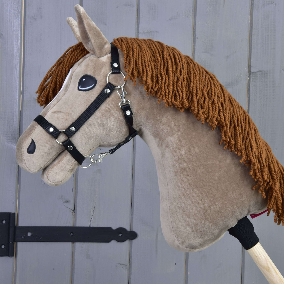 Side view of Hobby Horse Oliver wearing a black halter, the brown yarn mane falling along the neck, on a wooden stick