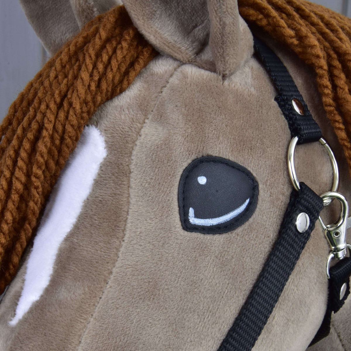 Close-up of Hobby Horse Oliver: black appliqué eye, white stripe, brown yarn mane and the silver ring of the black halter