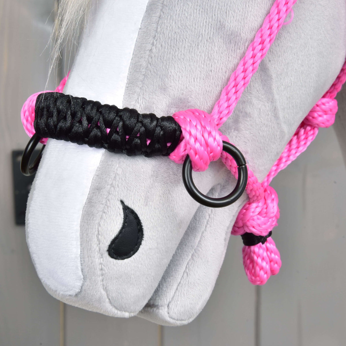 Close-up van de zwart gevlochten neusriem met zwarte ringen van de roze touwhalster op een grijze pluche neus