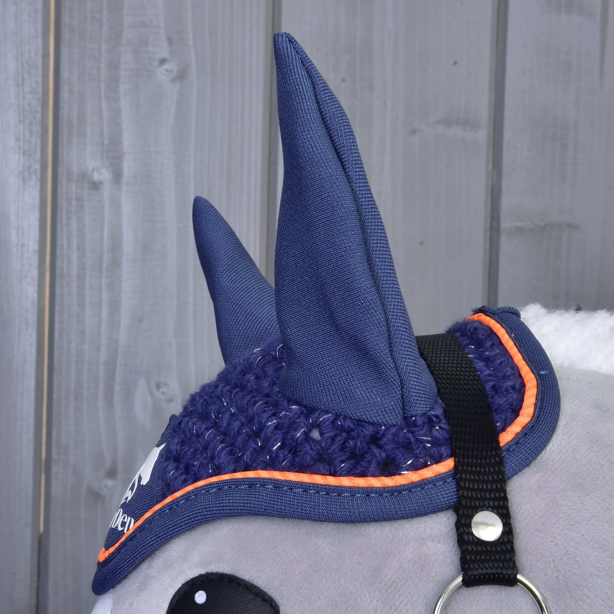 Gros plan sur les hautes oreilles bleu marine et le crochet bordé d’orange du bonnet d’oreilles Blue Sport, près de la sangle noire du licol