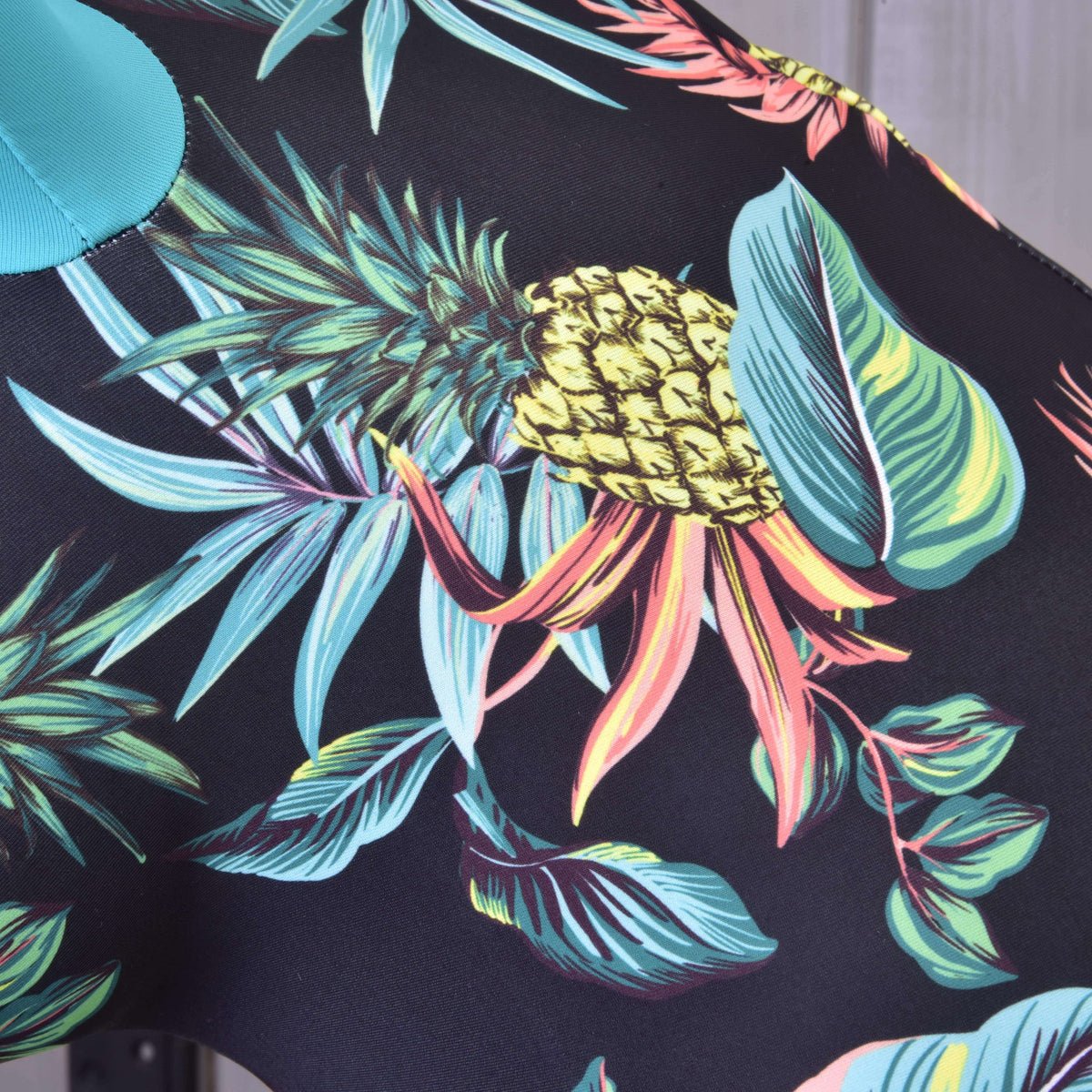 Detail van de print van Hobby Horse Beschermpak Pineapple: gele ananas, turquoise en koraalrode bladeren op zwarte Lycra