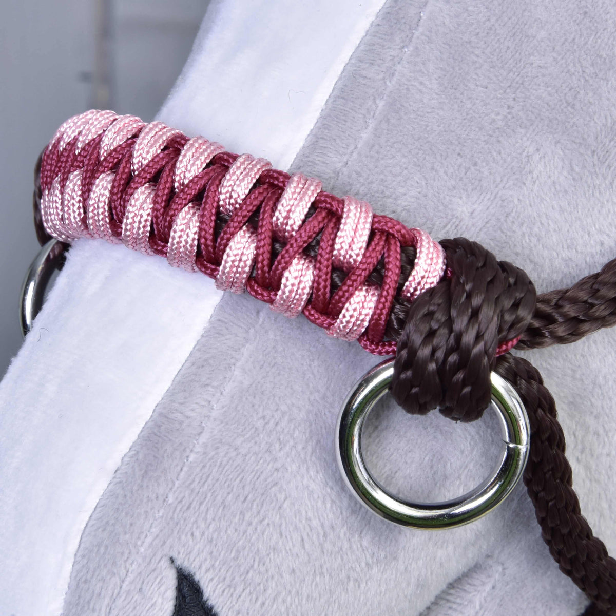 Gros plan sur la muserolle tressée rose et bordeaux avec anneau argenté et nœud marron foncé, sur un Hobby Horse