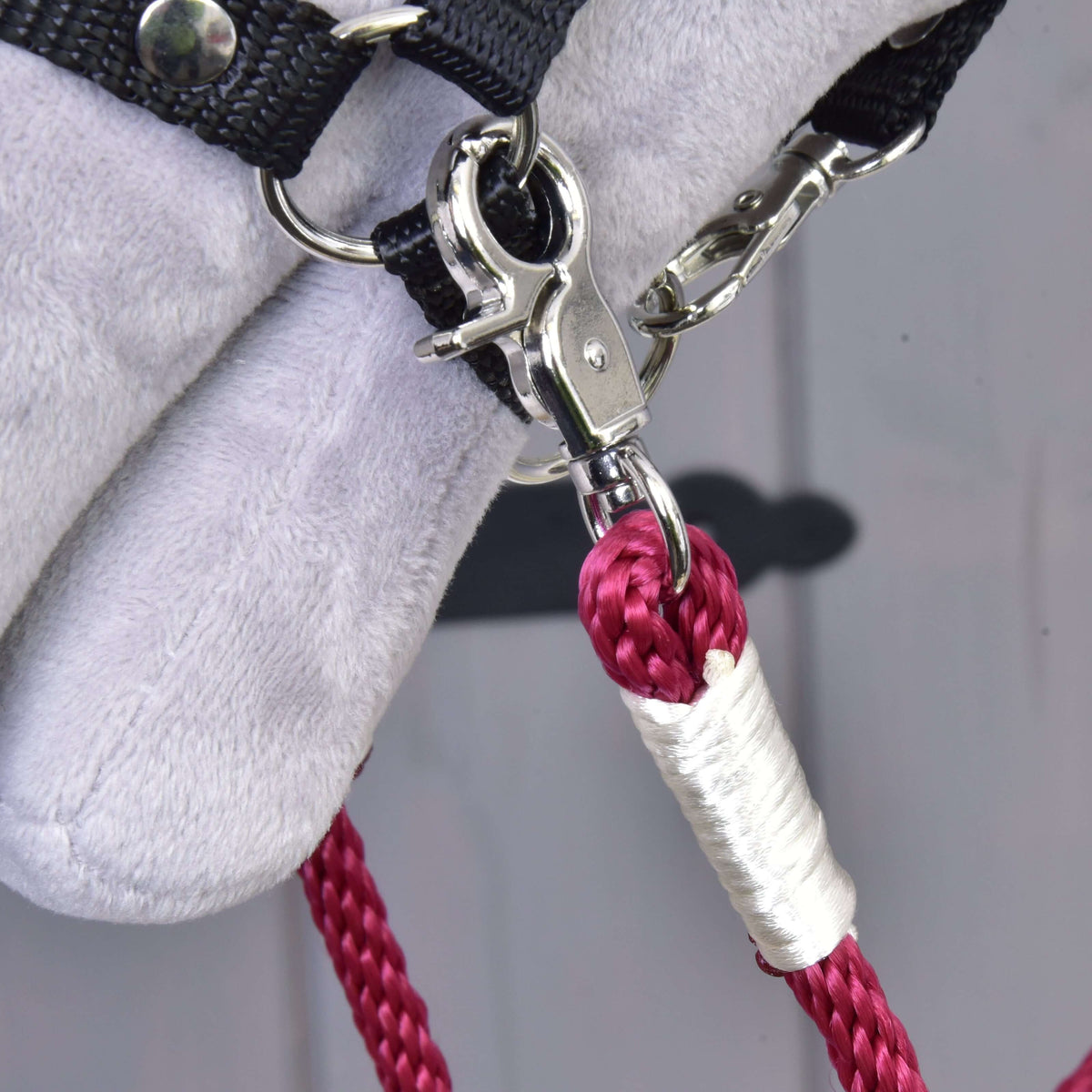 Gros plan sur le mousqueton argenté et la gaine blanche brillante des rênes en corde Czi-czi bordeaux, au licol d’un Hobby Horse