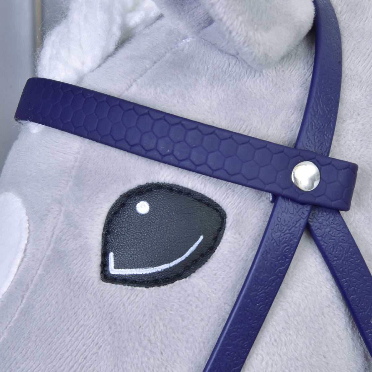Gros plan sur le frontal violet foncé motif nid d’abeille avec rivet argenté près de l’œil souriant d’un Hobby Horse gris