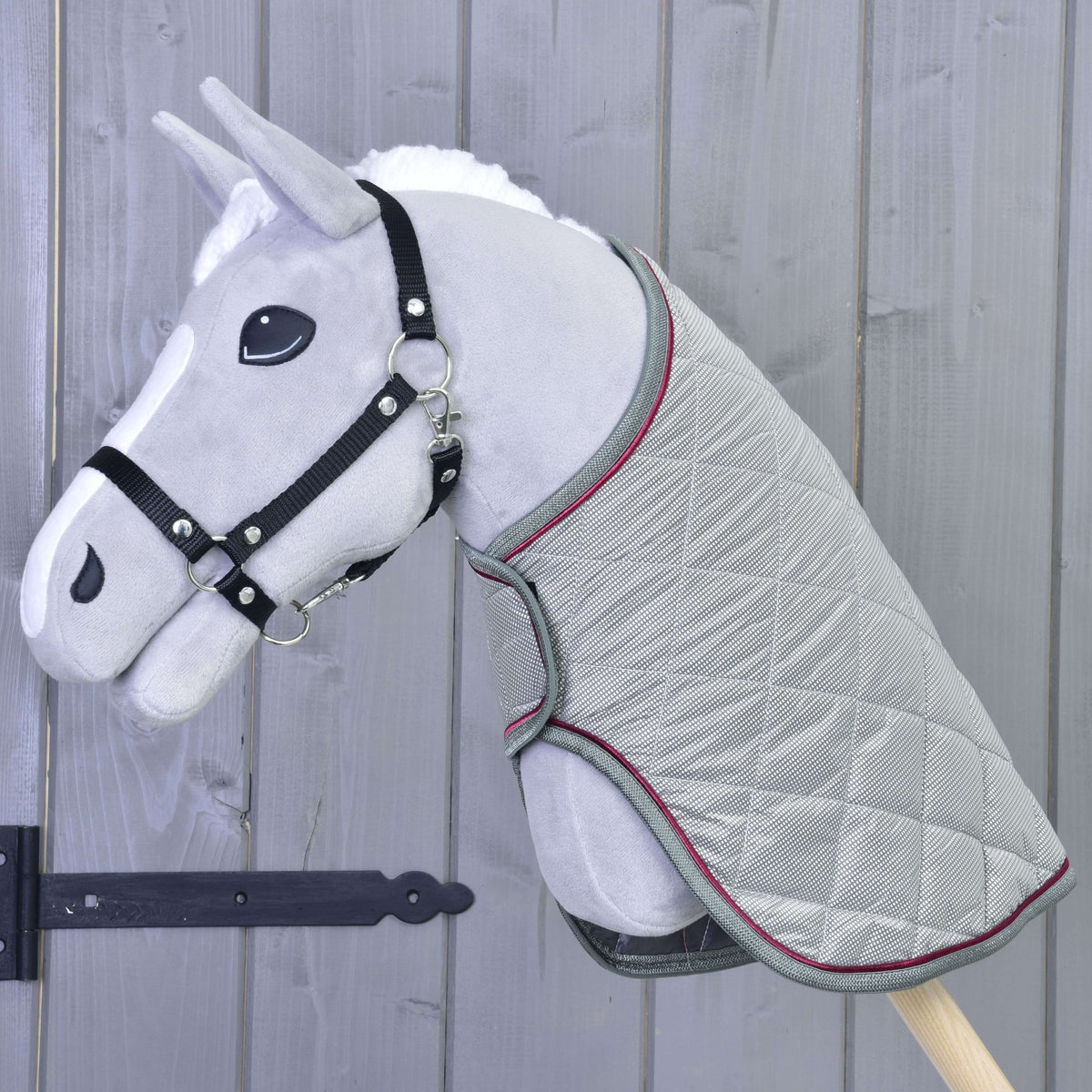 Lichtgrijze Hobby Horse met zwart halster draagt de gewatteerde zilvergrijze deken met grijze en frambozenrode rand