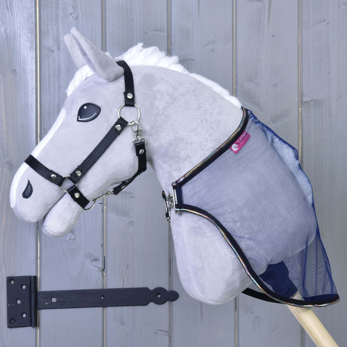 Hobby Horse gris avec licol noir portant la couverture anti-insectes en filet bleu marine, fermée au poitrail par une attache argentée