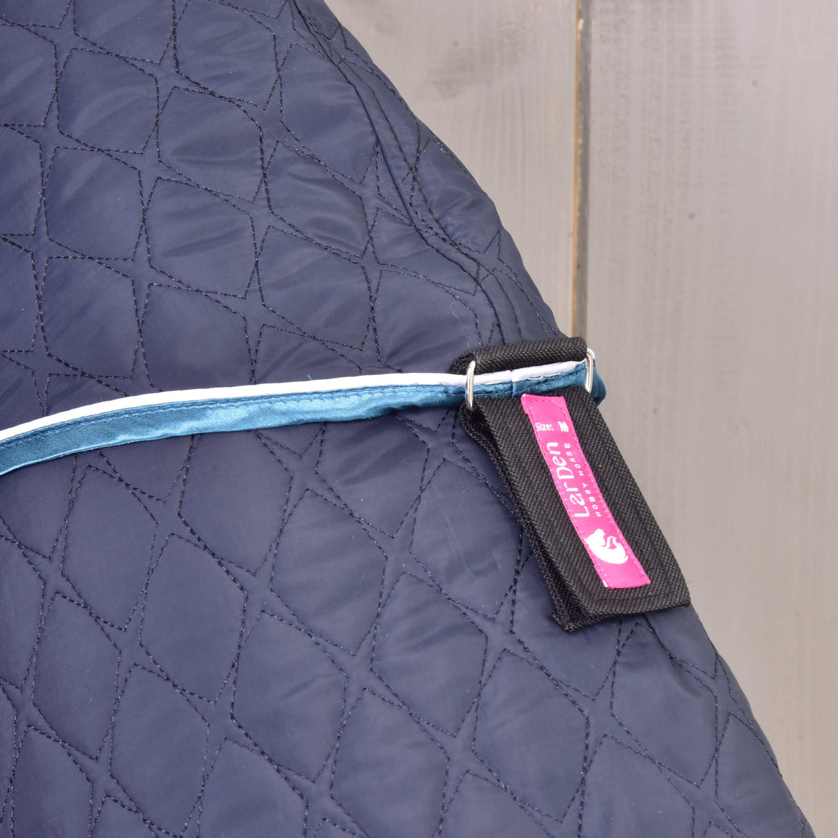 Close-up of a strap with pink LarDen label hanging from the blue trim of the navy quilted blanket on a Hobby Horse