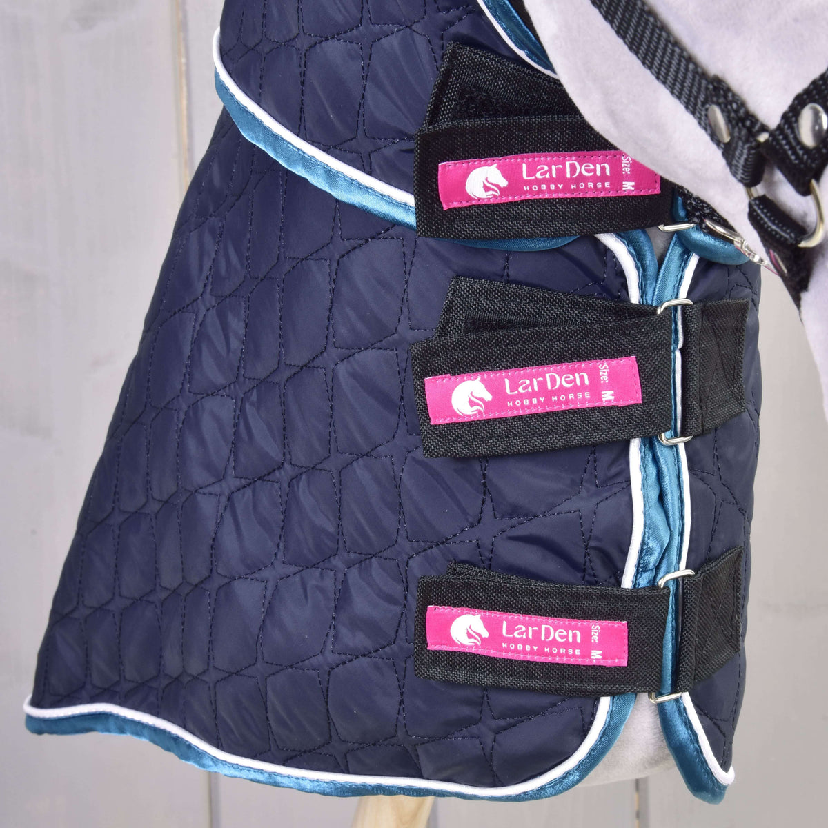 Close-up of the three LarDen Velcro straps closed at the chest of a grey Hobby Horse in the navy quilted blanket