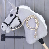 Crème-beige gevlochten halstertouw aan het zwarte halster van een grijze Hobby Horse voor een grijze houten wand