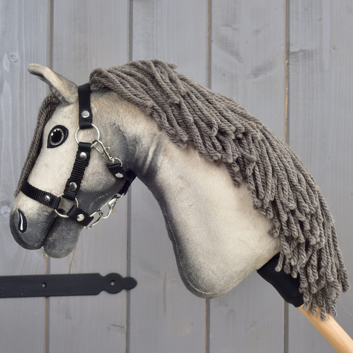 Hobby Horse Dusty facing left with the thick yarn mane draped over the neck down to the black grip of the stick