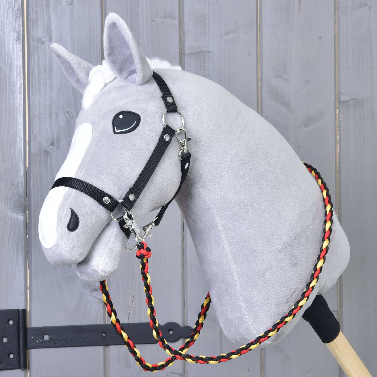 Lichtgrijze Hobby Horse met zwart halster en gevlochten zwart-rood-gele Teugels Flag om de hals