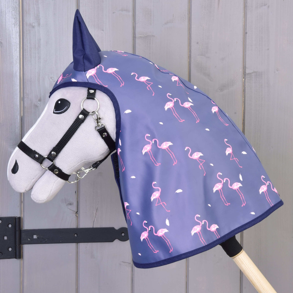 Zijaanzicht van de regenjas met flamingoprint over hoofd en hals van een grijze Hobby Horse voor een grijze houten wand