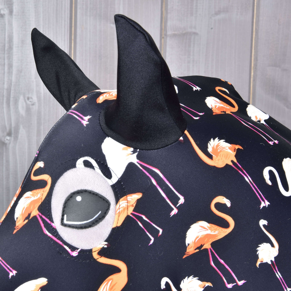 Close-up van de zwarte oren en de oogopening in het Lycra-pak met flamingoprint op een grijze Hobby Horse
