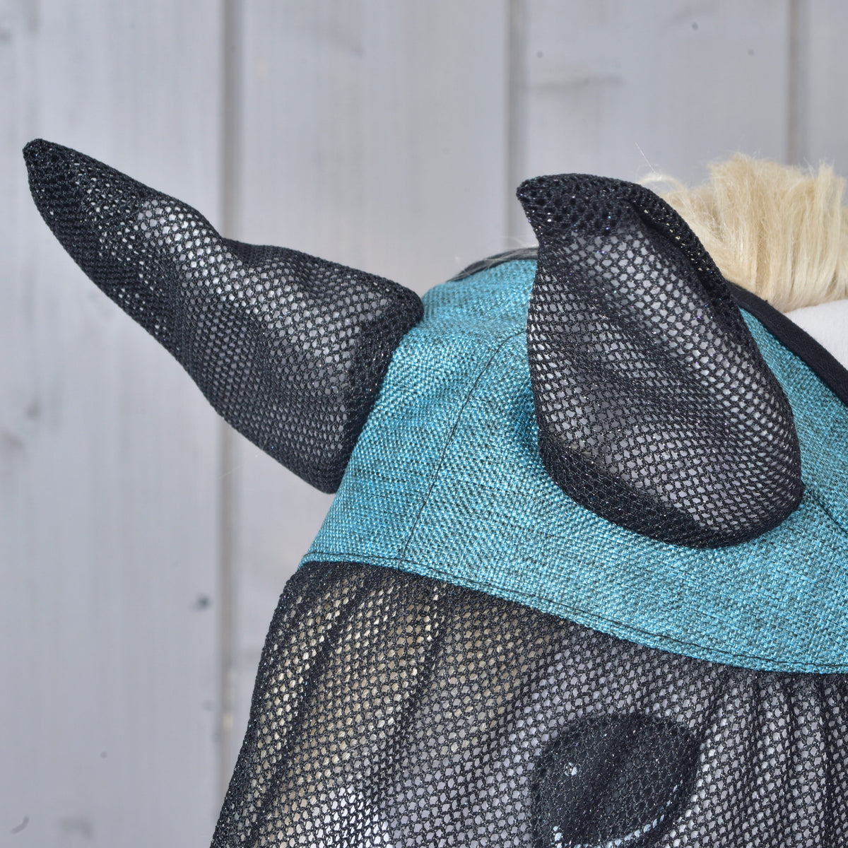 Close-up of the black mesh ear covers and textured turquoise crown panel of the fly mask on a grey Hobby Horse
