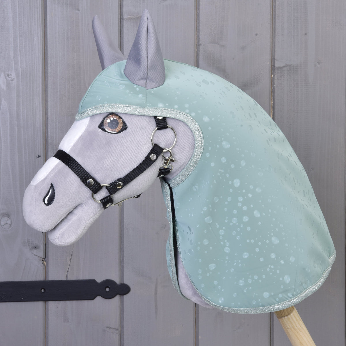 Hobby Horse gris avec licol noir portant l’imperméable vert menthe à motif de gouttes et oreilles grises