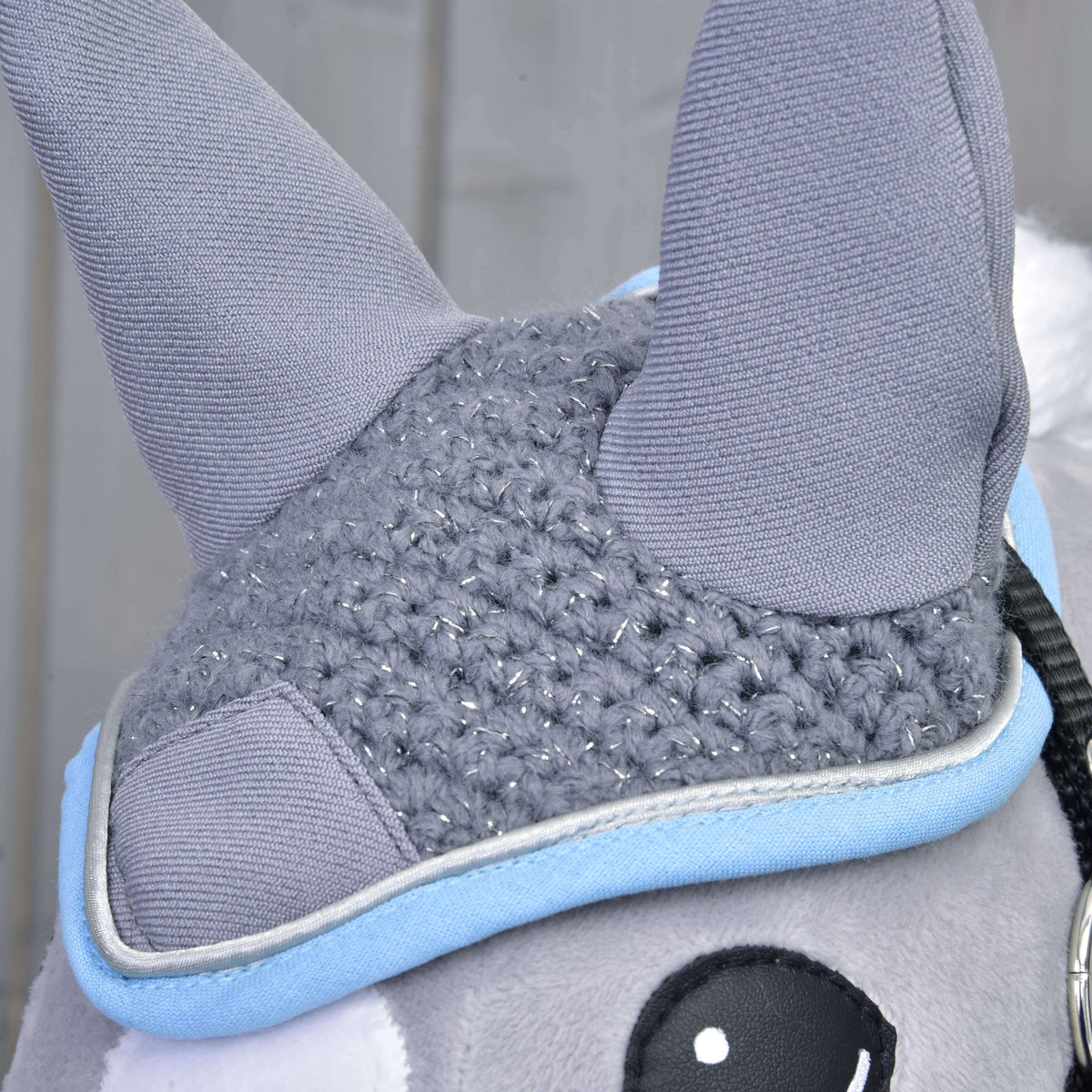 Detail van het gehaakte grijze oornetje op een Hobby Horse: glinsterende steken, grijze oren en blauw-zilveren rand