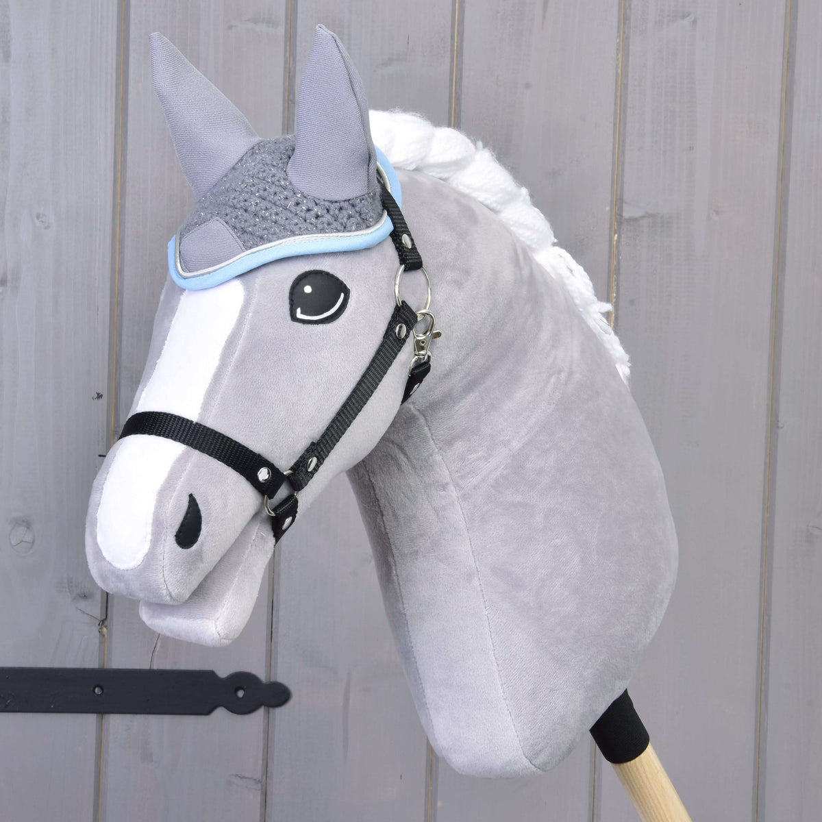 Grijze Hobby Horse met witte gevlochten manen en zwart halster draagt het gehaakte grijze oornetje met lichtblauwe bies