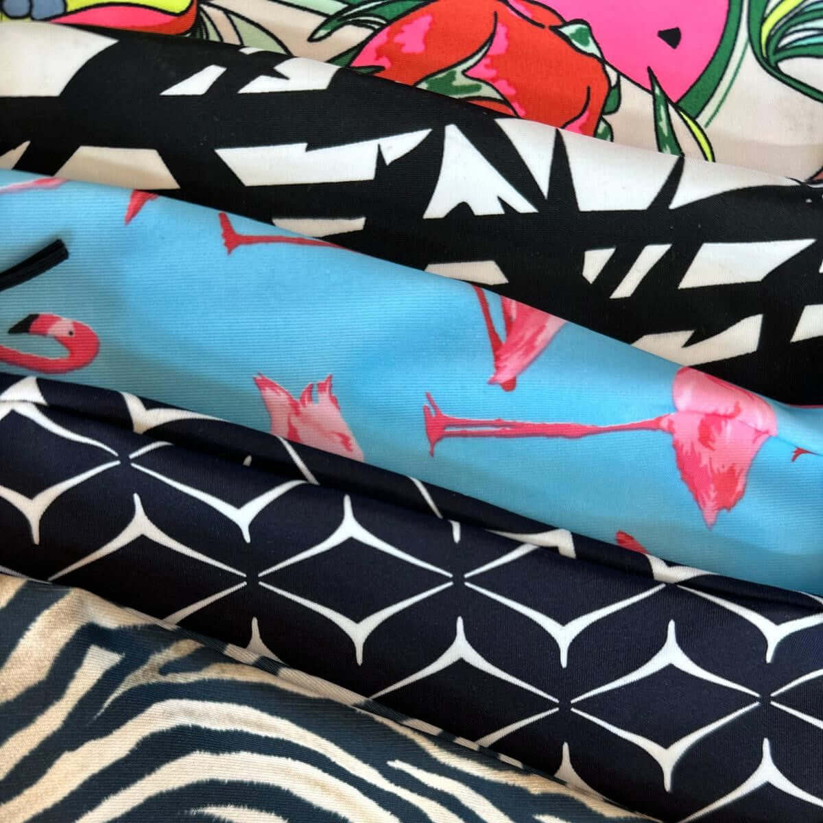 Five stacked fabrics: tropical fruit print, black and white abstract, pink flamingos on blue, navy geometric and zebra